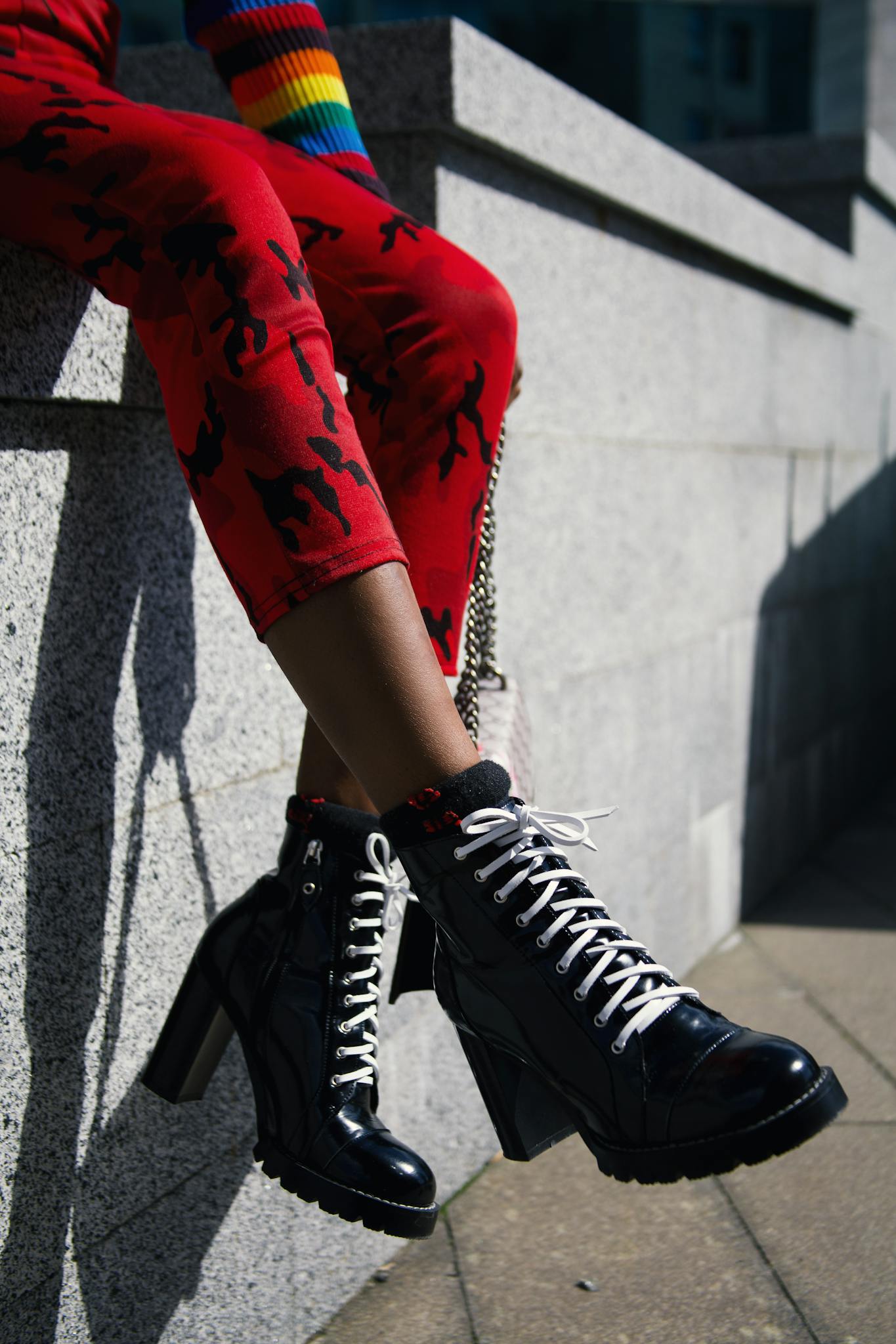 Trendy black boots and red pants with colorful sleeve in urban setting, showcasing unique fashion style.